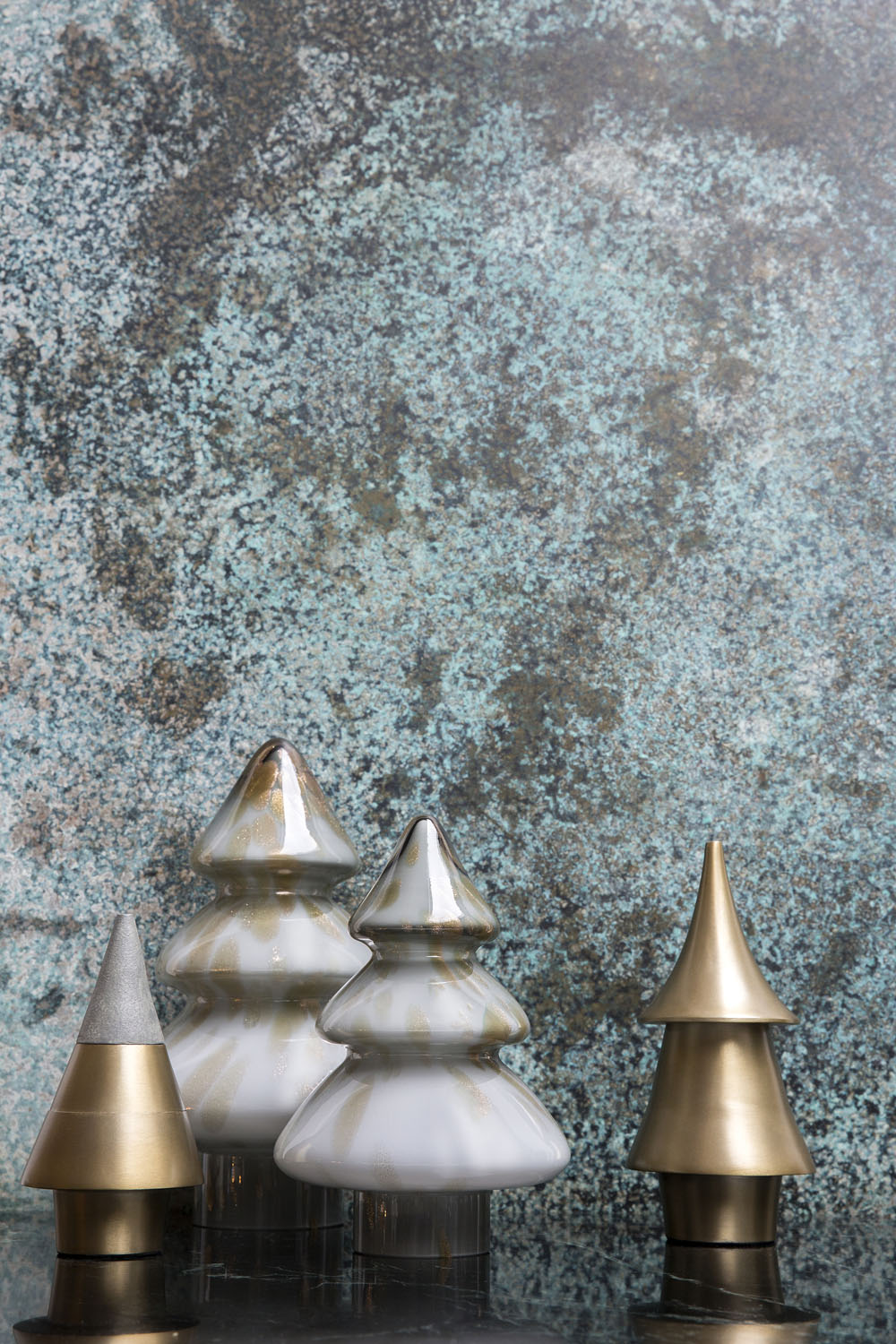 Four decorative tree-shaped ornaments, two metallic gold and two white with gold streaks, are arranged in front of a textured blue and brown background.